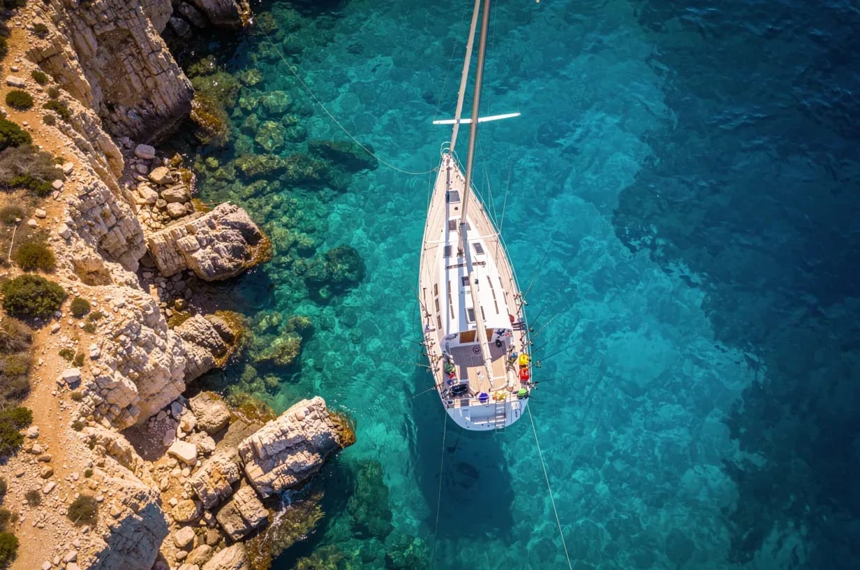 Aerial view of a sailboat anchored in a rocky cove in Alicante with fishing rods on deck