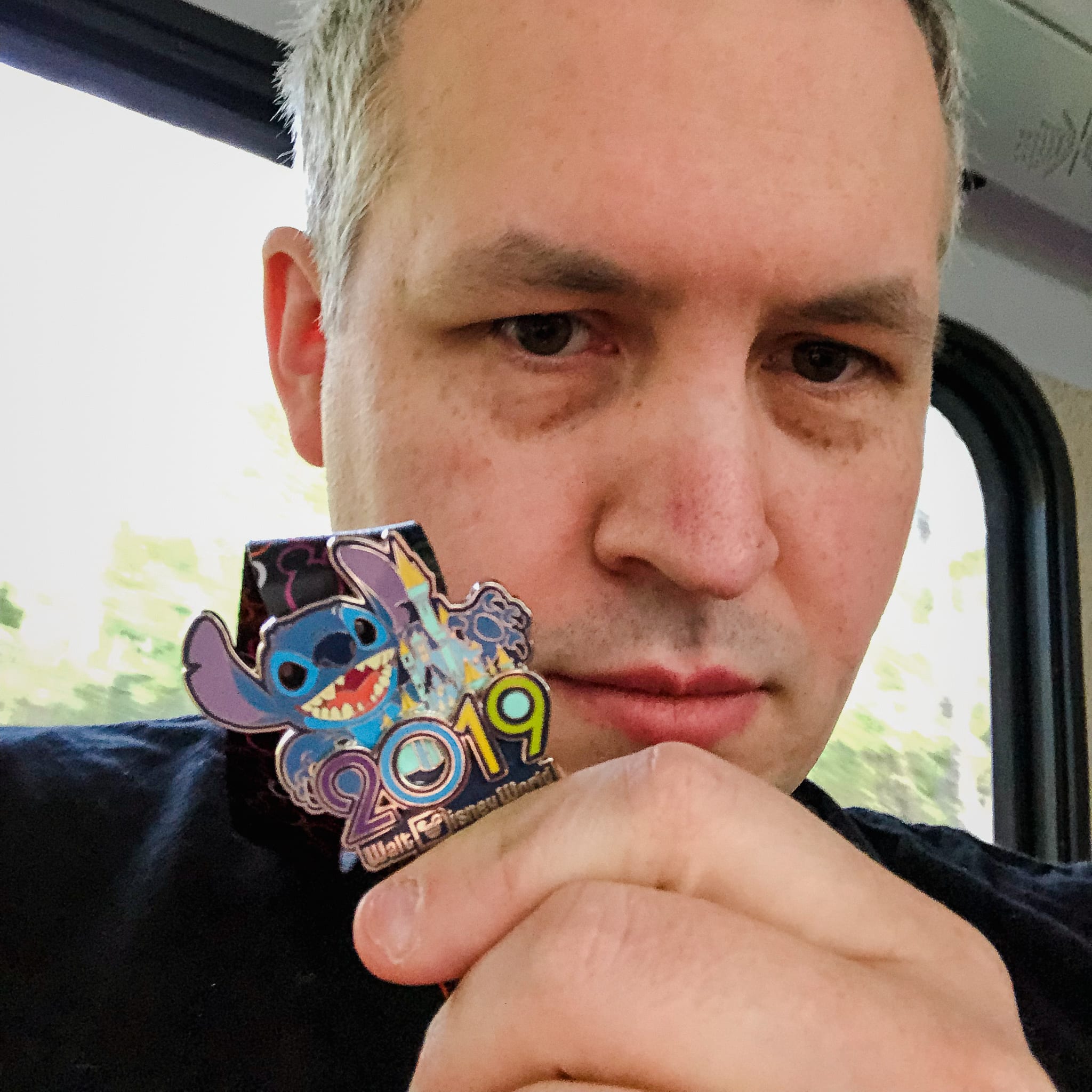 Photo of David Demaree holding up a Disney World "2019" pin featuring Stitch