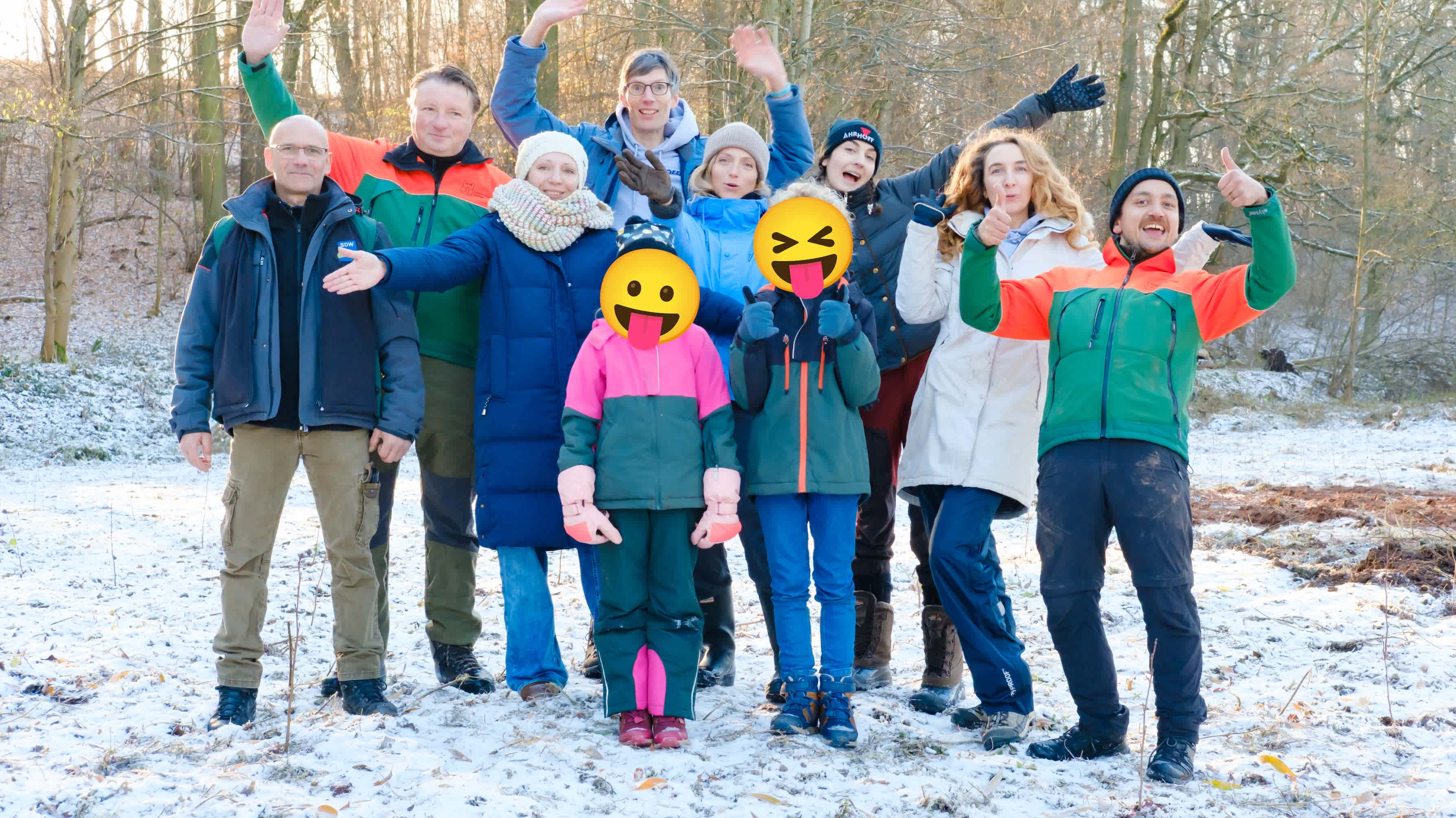 Group cheering for a joint photo. Some planted young trees can be seen in the ground, with forest in the background.