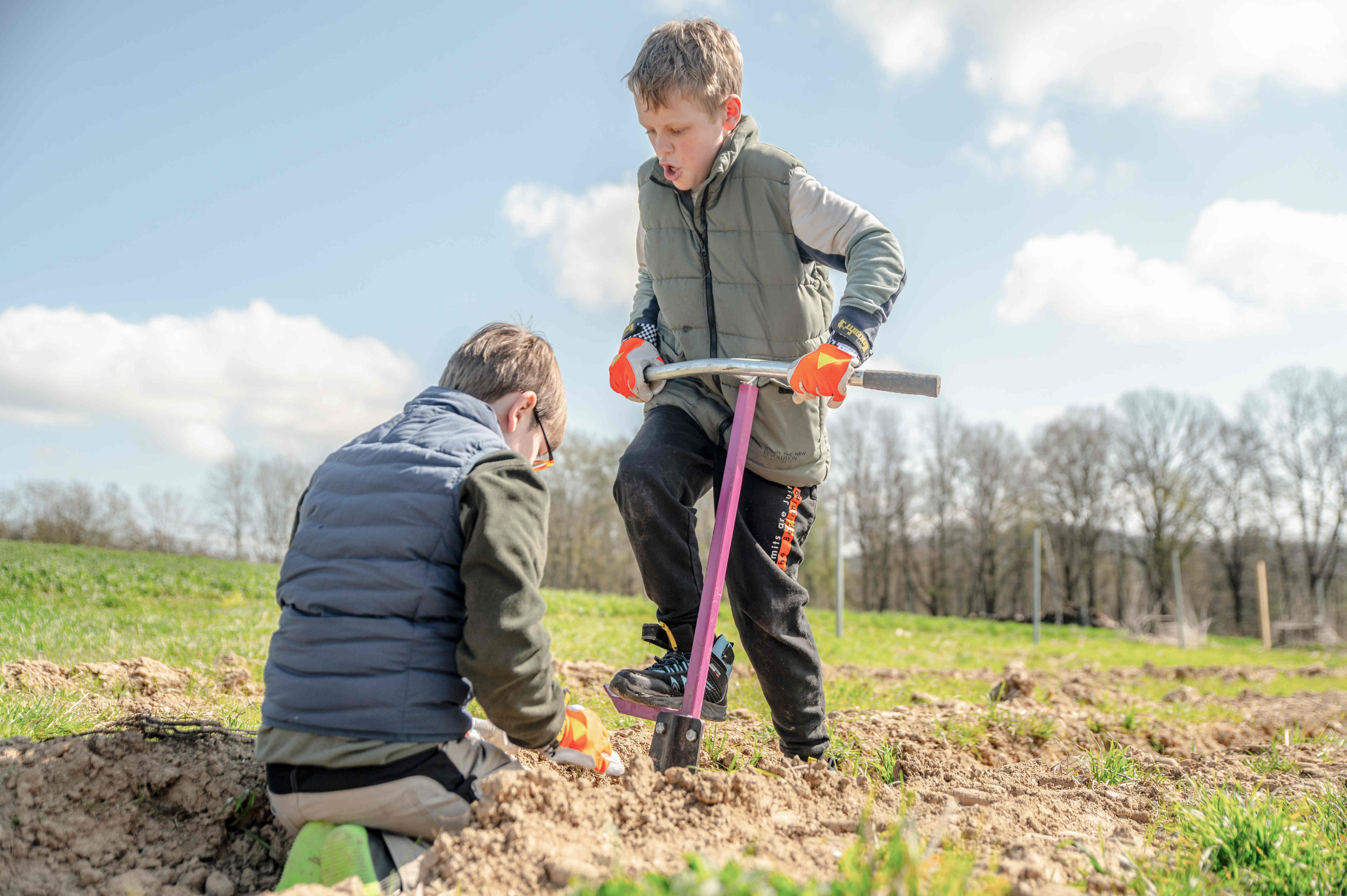 Zwei Kinder pflanzen zusammen. Das Kind rechts drückt kräftig den Pflanzspaten in die Erde.