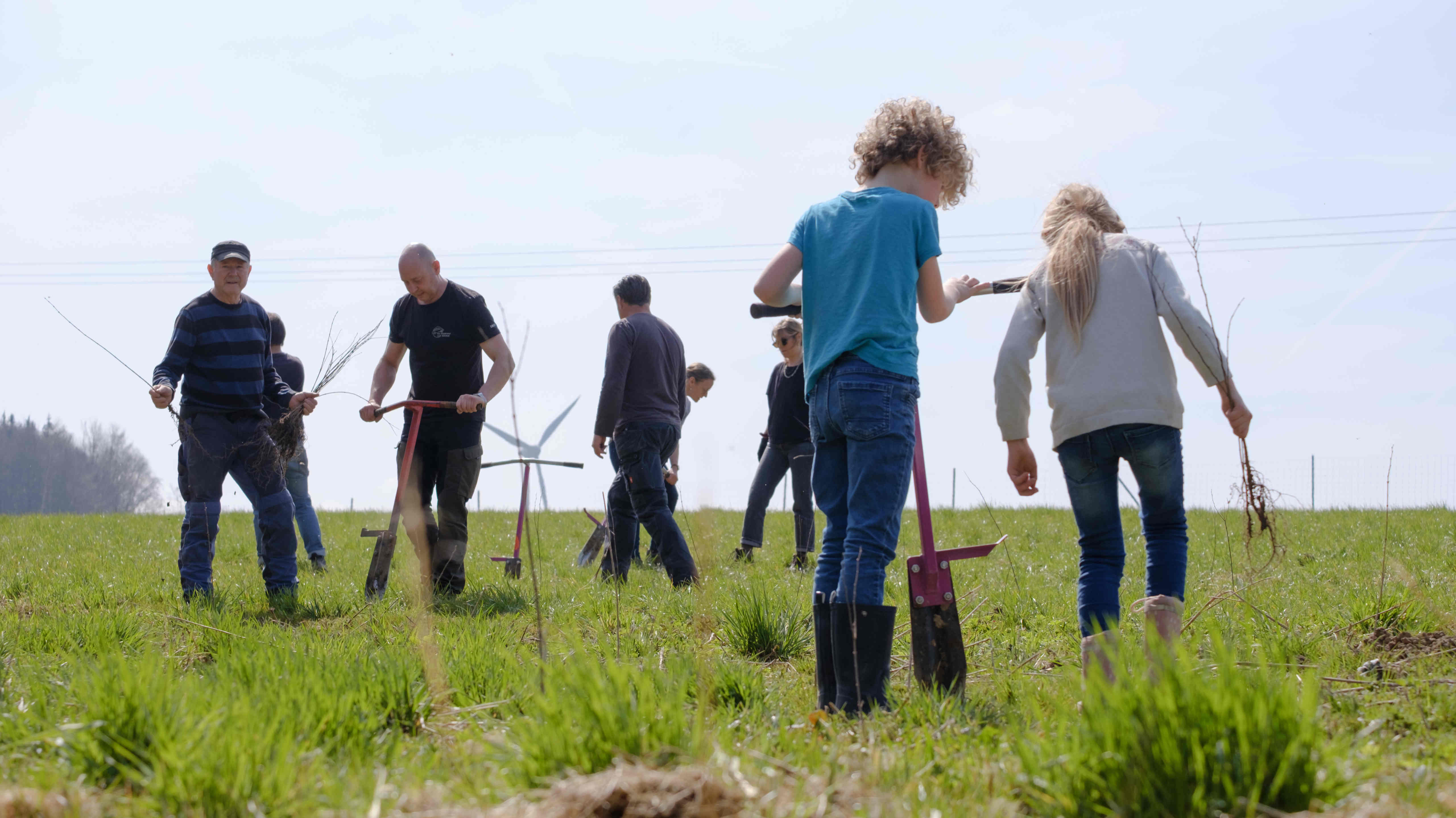 People of various ages working on a field with planting spades. Two children in the foreground.