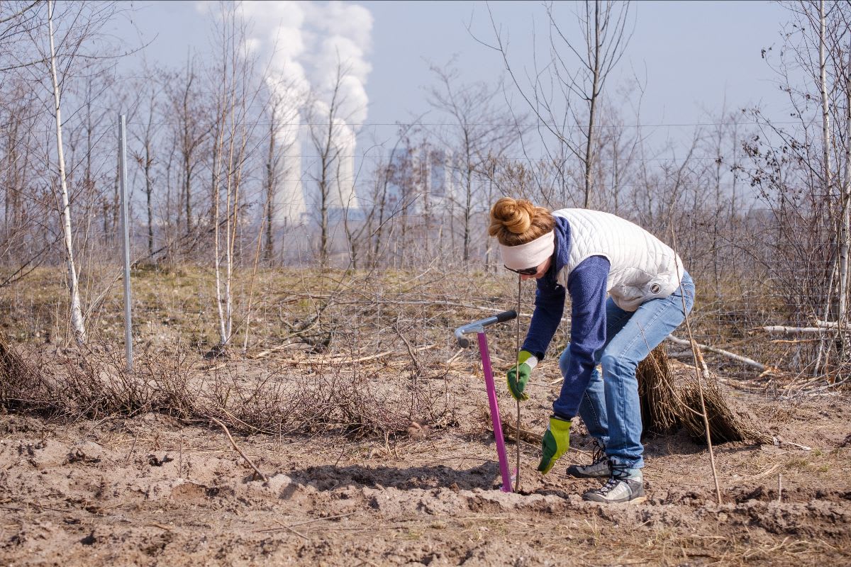 Foto von Ruth, der Gründerin von ForTomorrow, wie sie einen Baum pflanzt, im Hintergrund siehst du ein Kohlekraftwerk  CO₂ Ausstoß