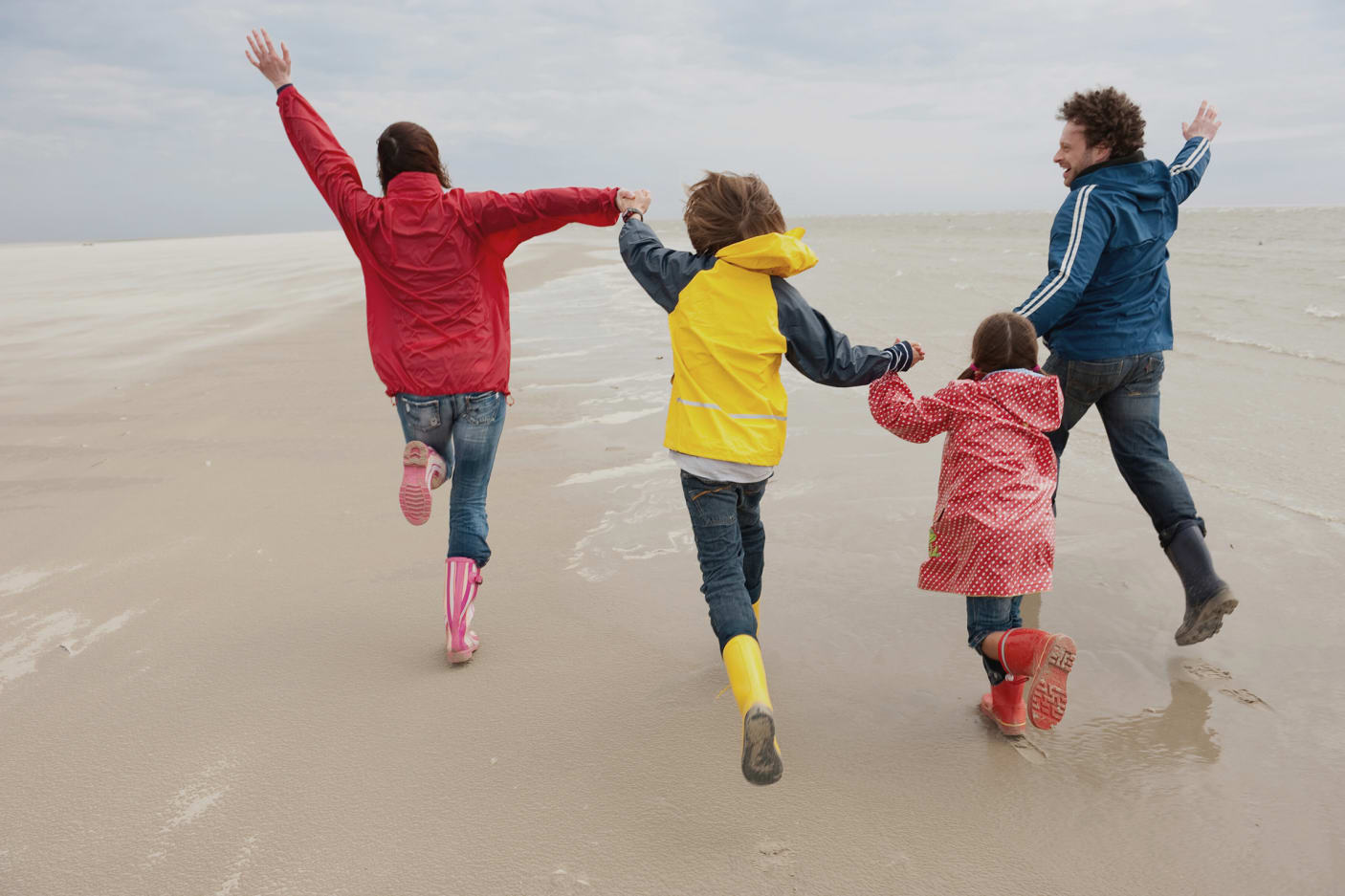 Mutter, Vater und zwei Kinder von hinten, fröhlich springend, an der Nordsee.