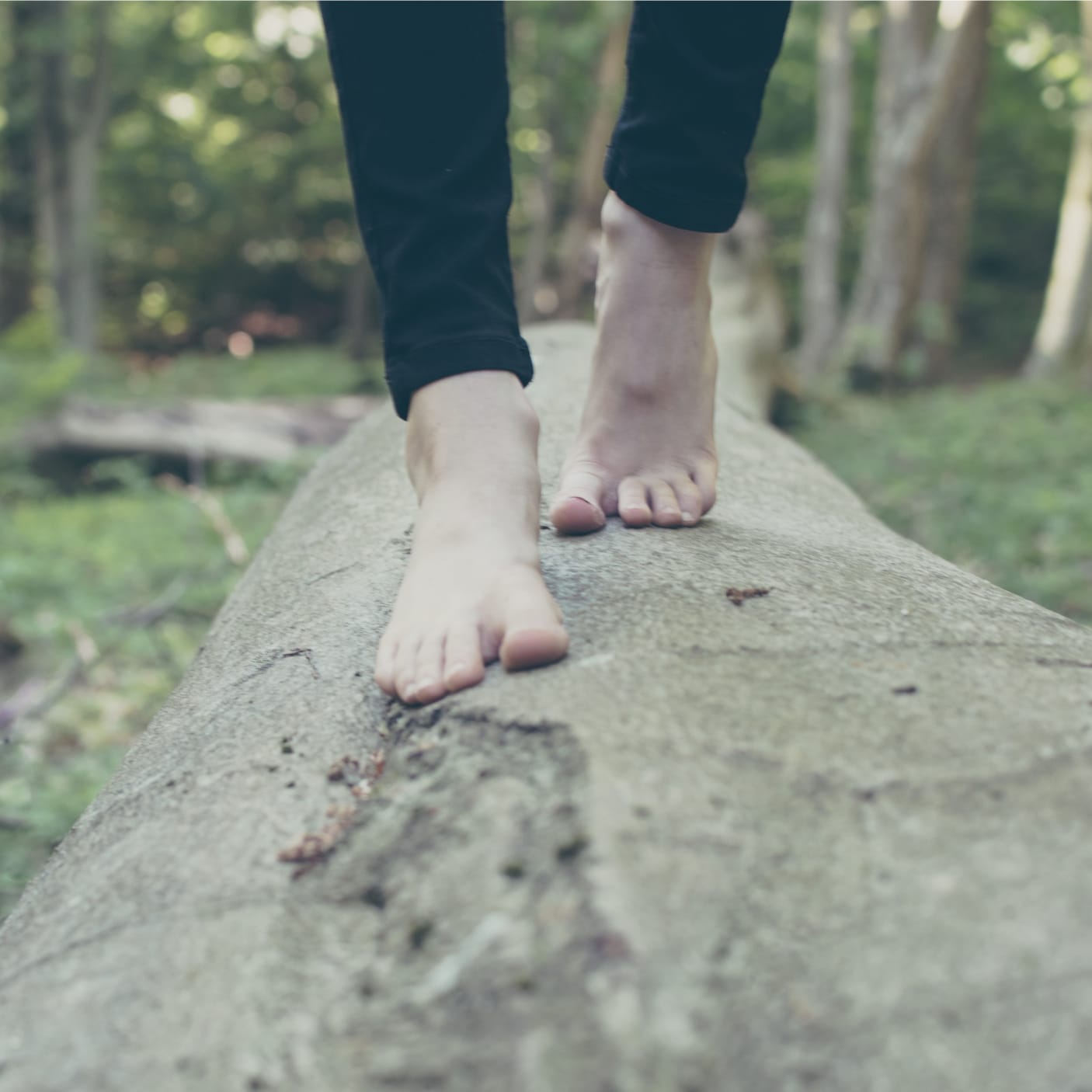 woman walking barefoot on a tree trunk in the forest