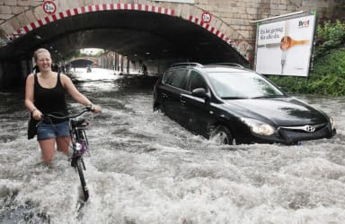 A street that is under water, a woman walks through the water with her bicycle.