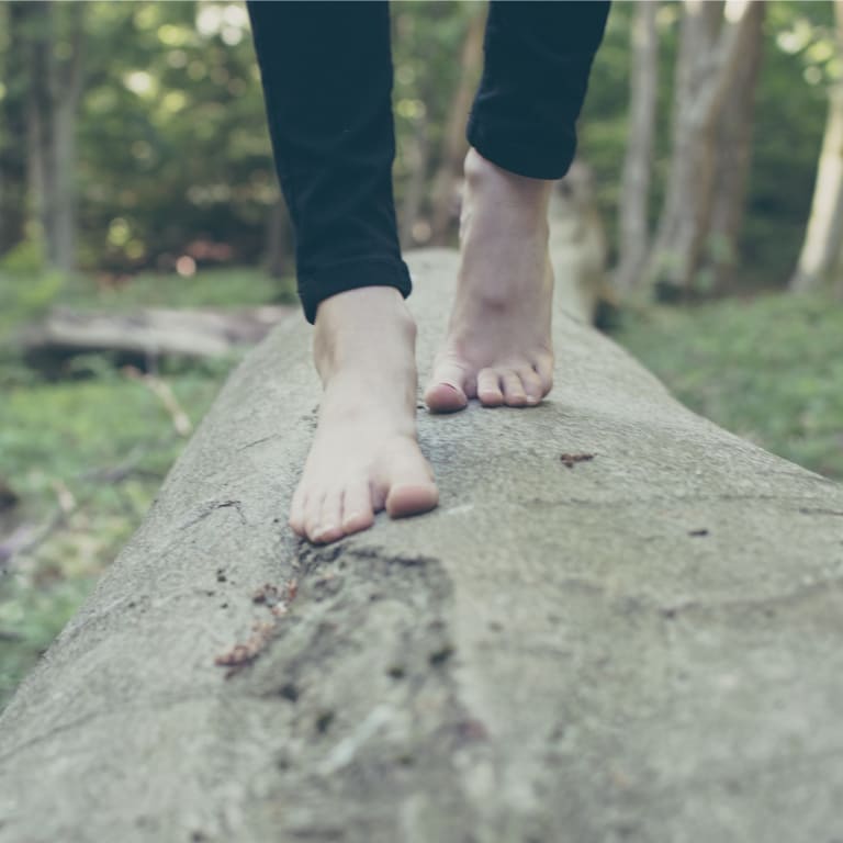 frau läuft barfuß auf einem baumstamm im wald