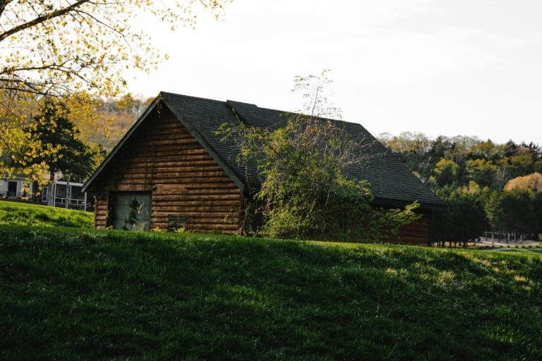 Foto einer kleinen Holzhütte hinter einem Hügel auf einer grünen Wiese.