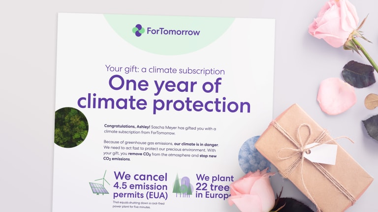 Gift table with roses and a printed certificate of a climate subscription gift. The text on it is: Your gift: a climate subscription. Climate neutral for one year. Underneath text that is too small to read. But still visible is: 'We delete 4.5 emission rights (EUA)' and 'We plant 22 trees in Germany'.