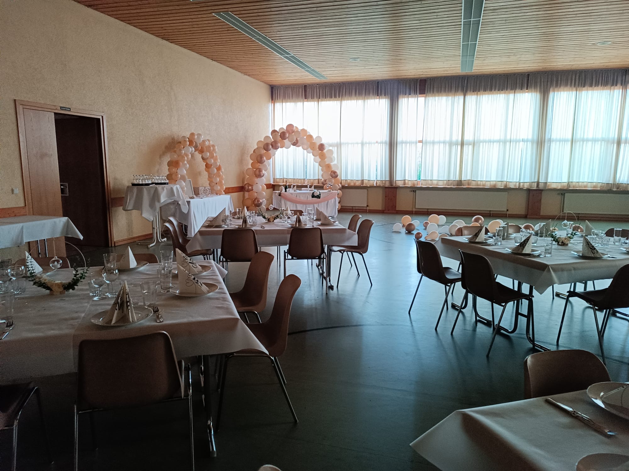 Gedeckte Tischinseln mit Stühlen verteilt in der RVB Halle, im Hintergrund ein besonders geschmückter Tisch für das Brautpaar