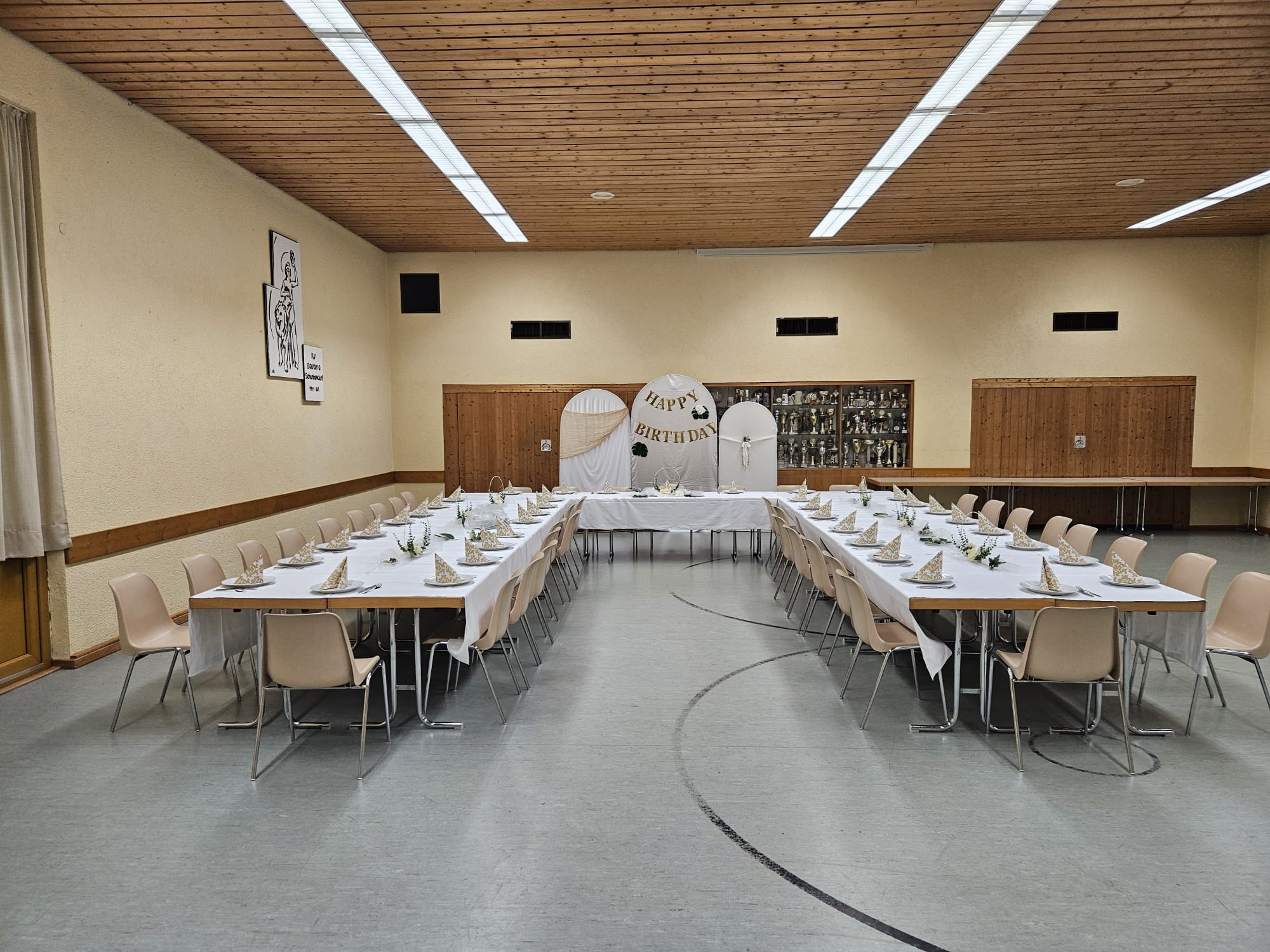 In U-Form zusammengestellte und gedeckte Tische mit Stühlen in der RVB Halle, im Hintergrund ein großes „Happy Birthday“-Schild
