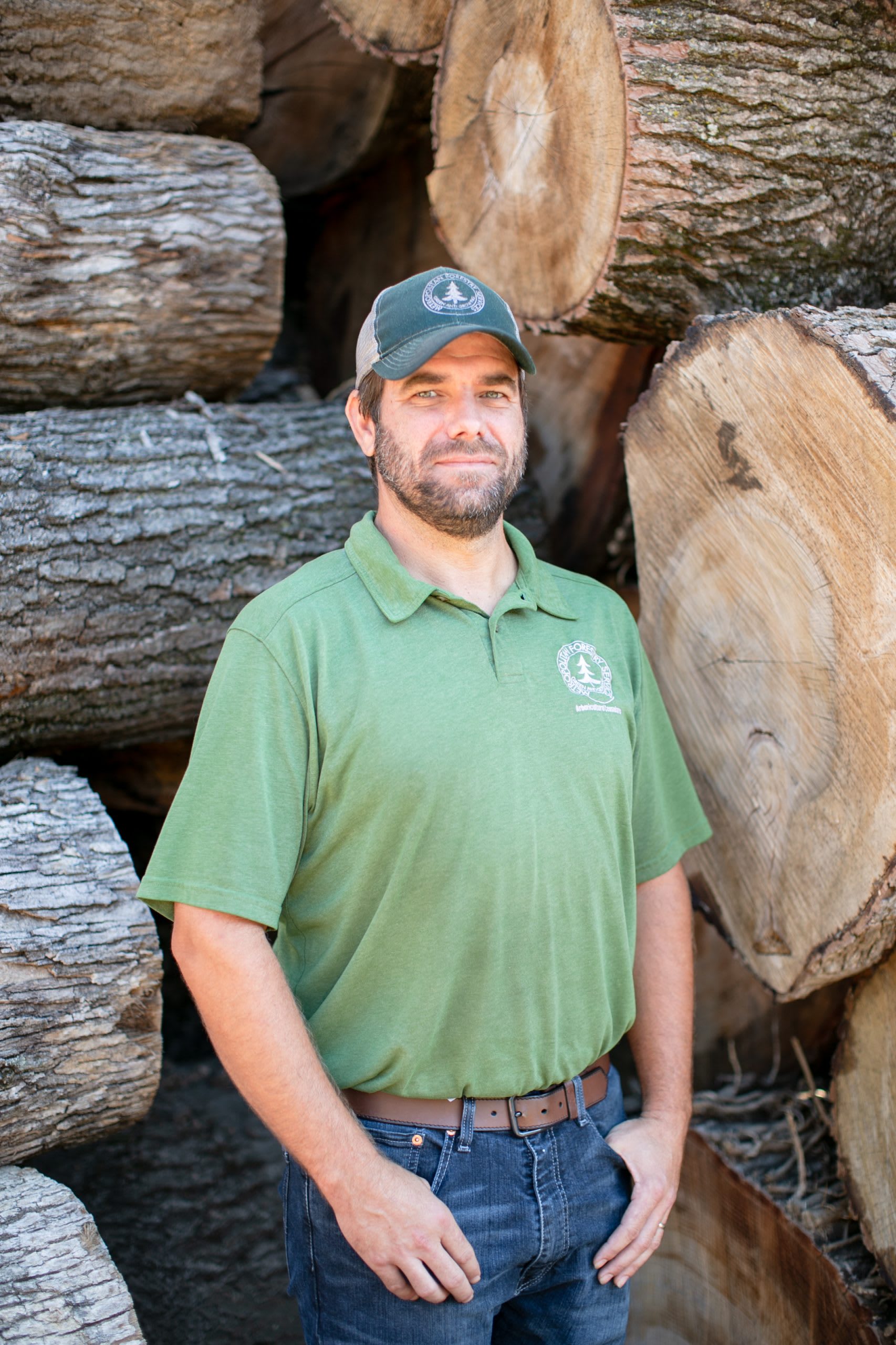 Man in a green shirt standing in front of tree logs.