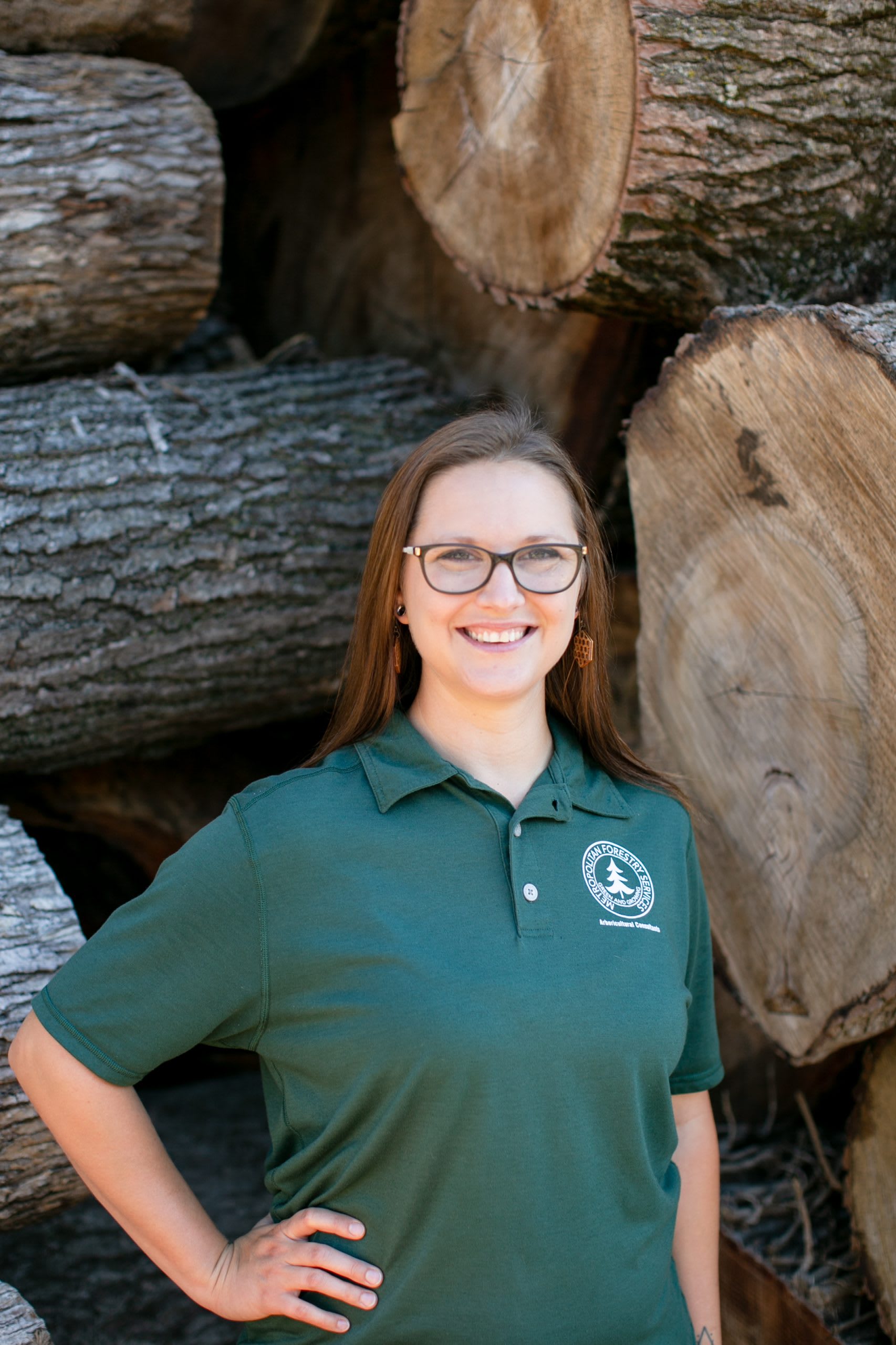 Woman in a dark green shirt standing in front of tree logs.