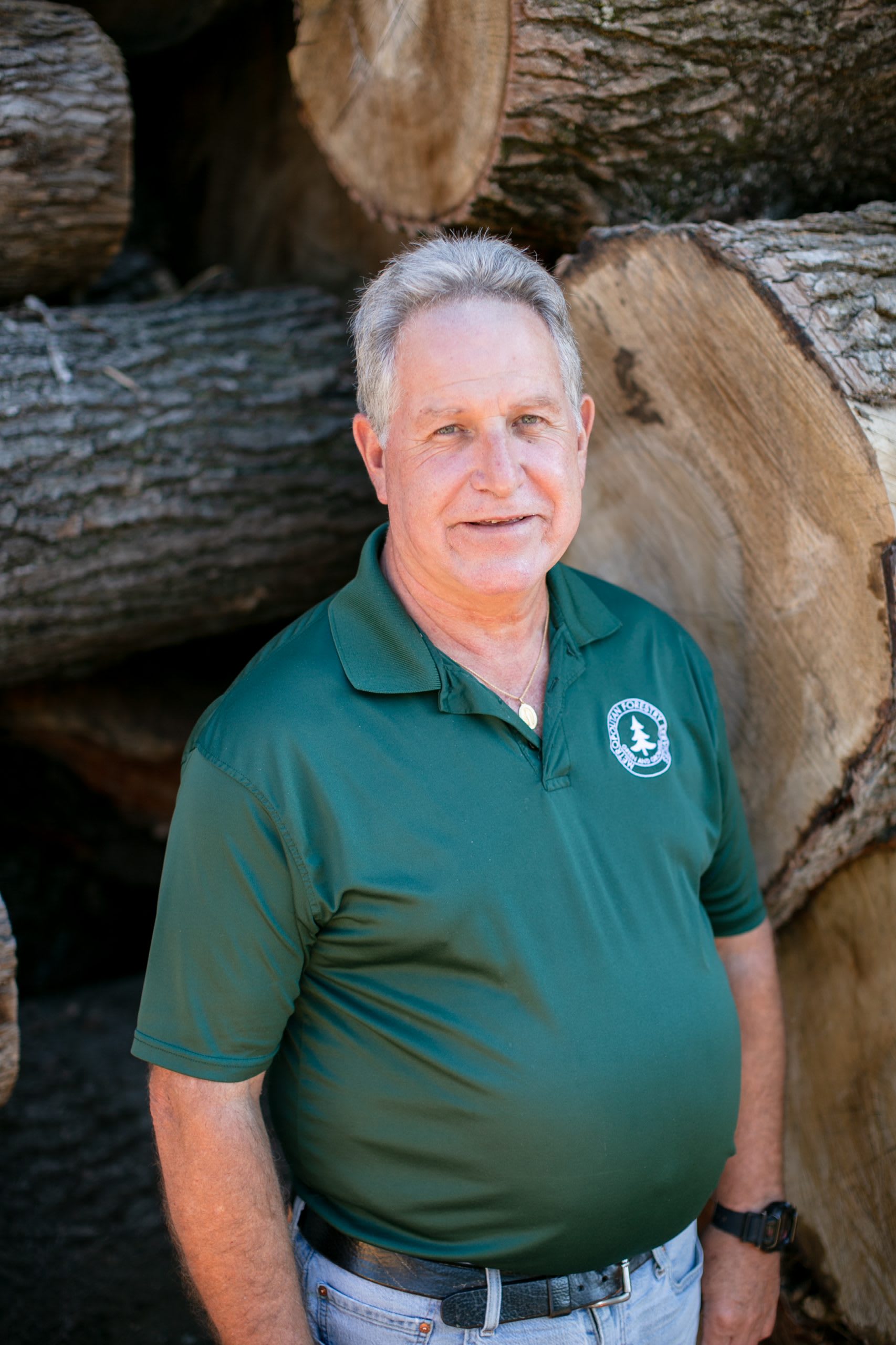 Man wearing dark green shirt standing in front of tree logs