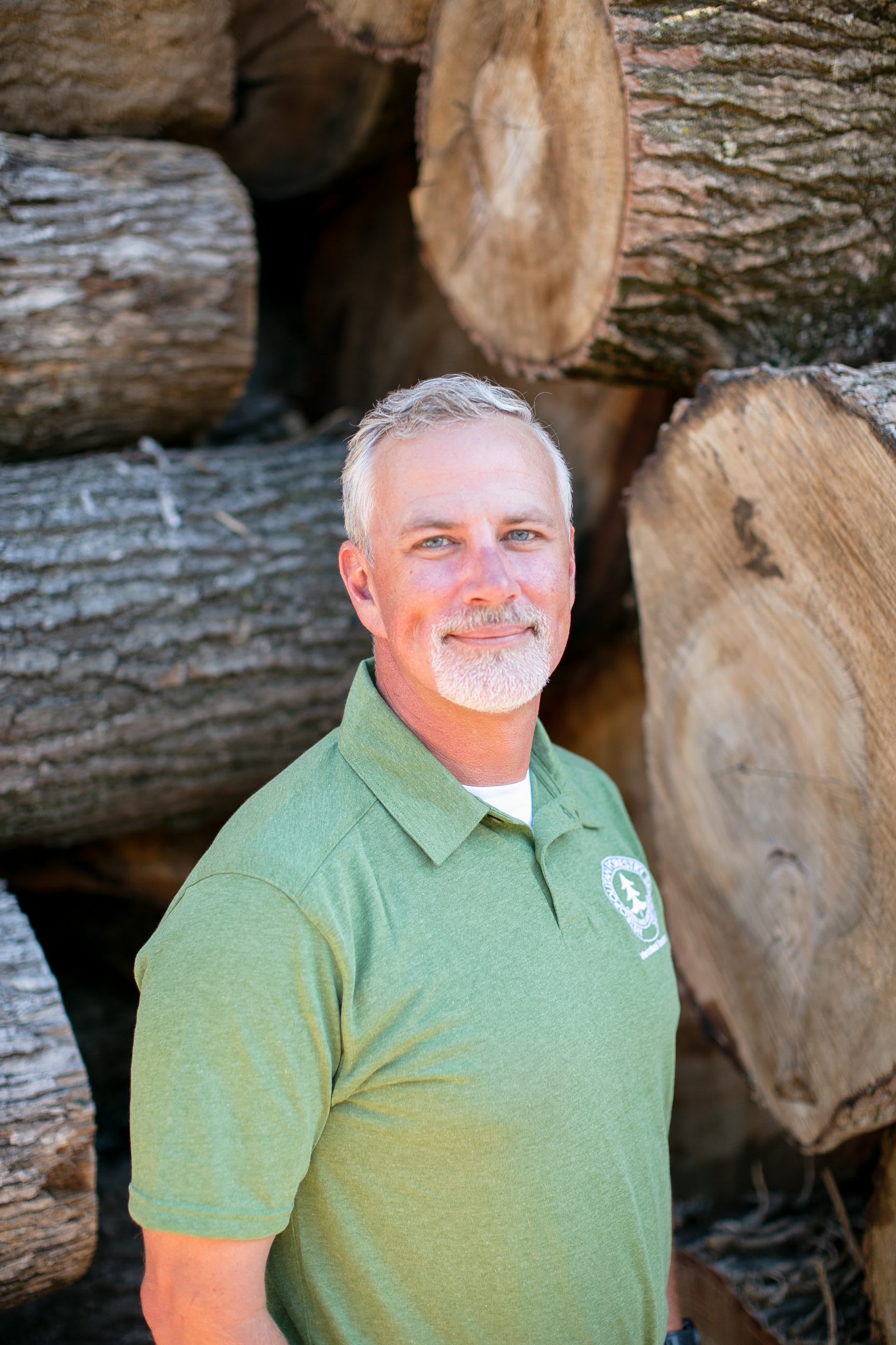 Man wearing light green shirt standing in front of tree logs.