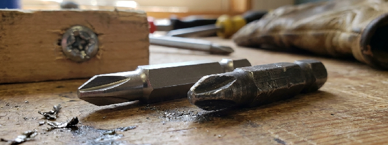 Versleten bits naast nieuwe bit, close-up van slijtage aan bitpunt en beschadigde schroefkop