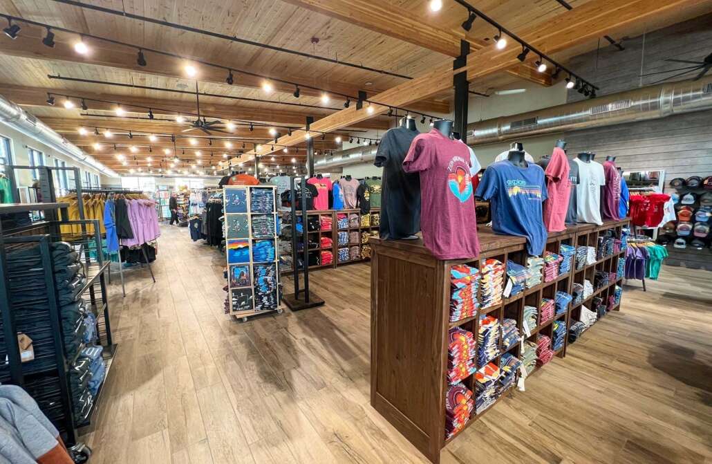 Retail store with wooden displays of folded t-shirts, hats, and apparel racks on mannequins