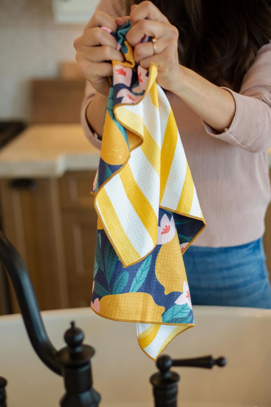 Woman holding a colorful striped and floral kitchen towel over a farmhouse sink