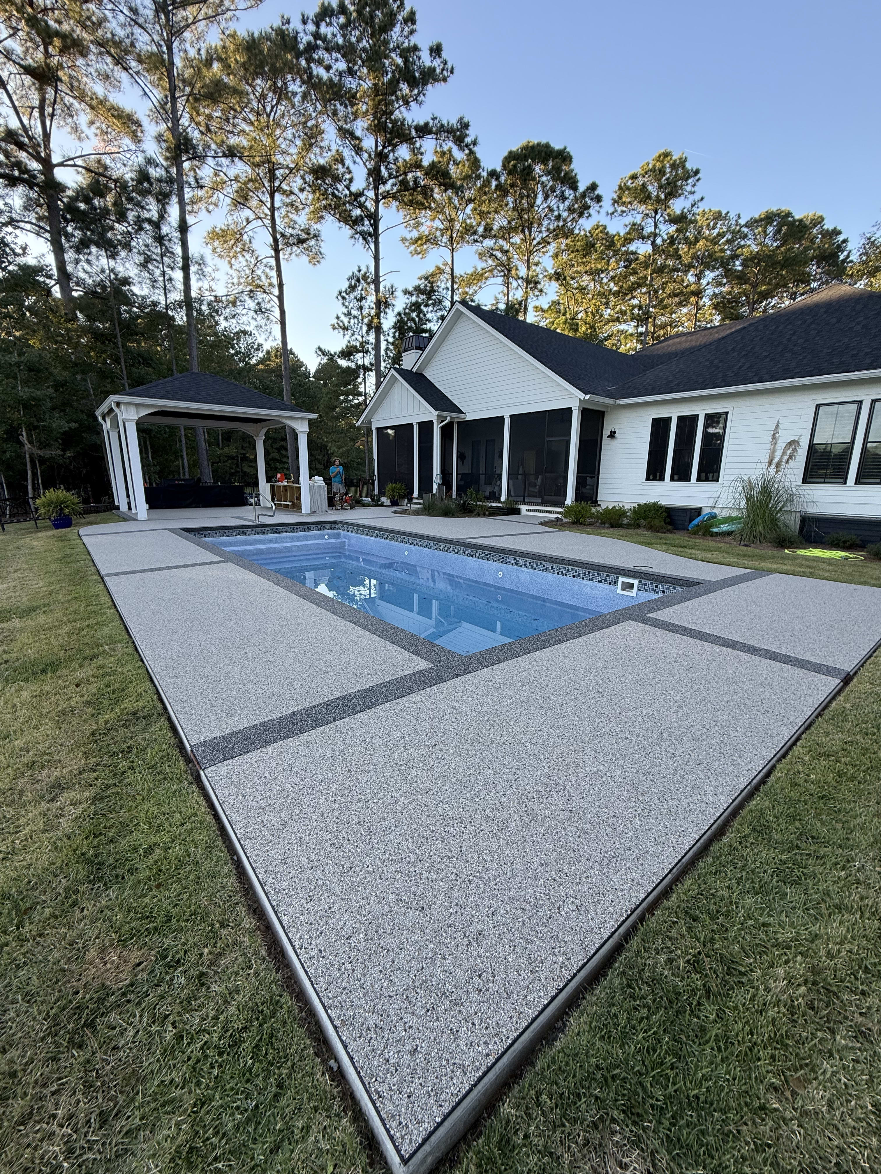 A textured stone patio surrounding a blue pool with a gazebo and trees in May River.