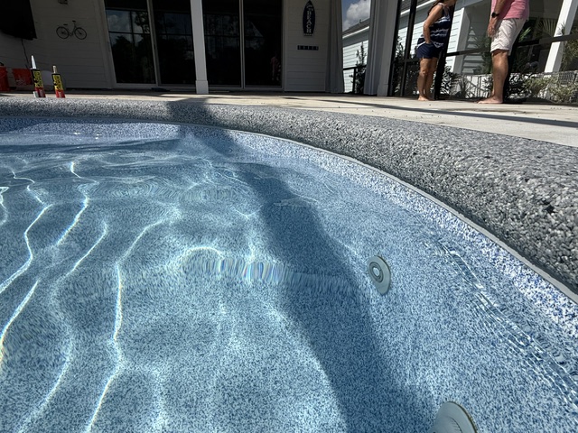A close-up view of a resin-bound pool deck coating with clear water and people in the background.