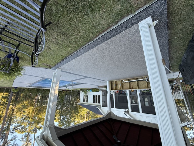 A covered patio showcasing a resin-bound deck beside a clear blue pool and a house.