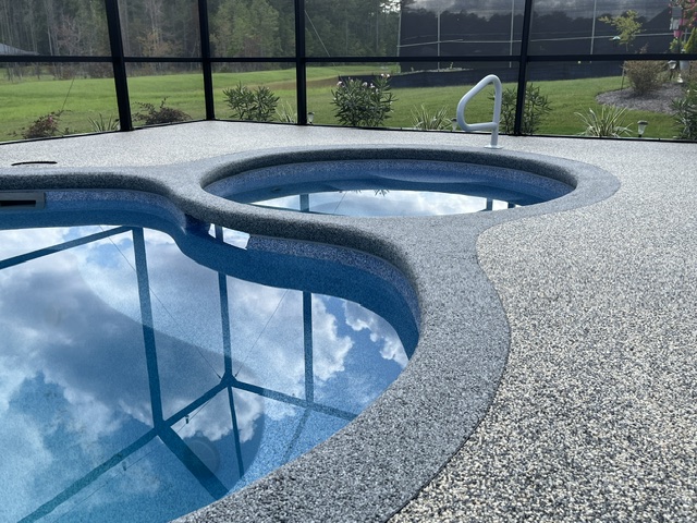 A curved pool deck with a reflective surface and a clear blue pool under a screened enclosure.
