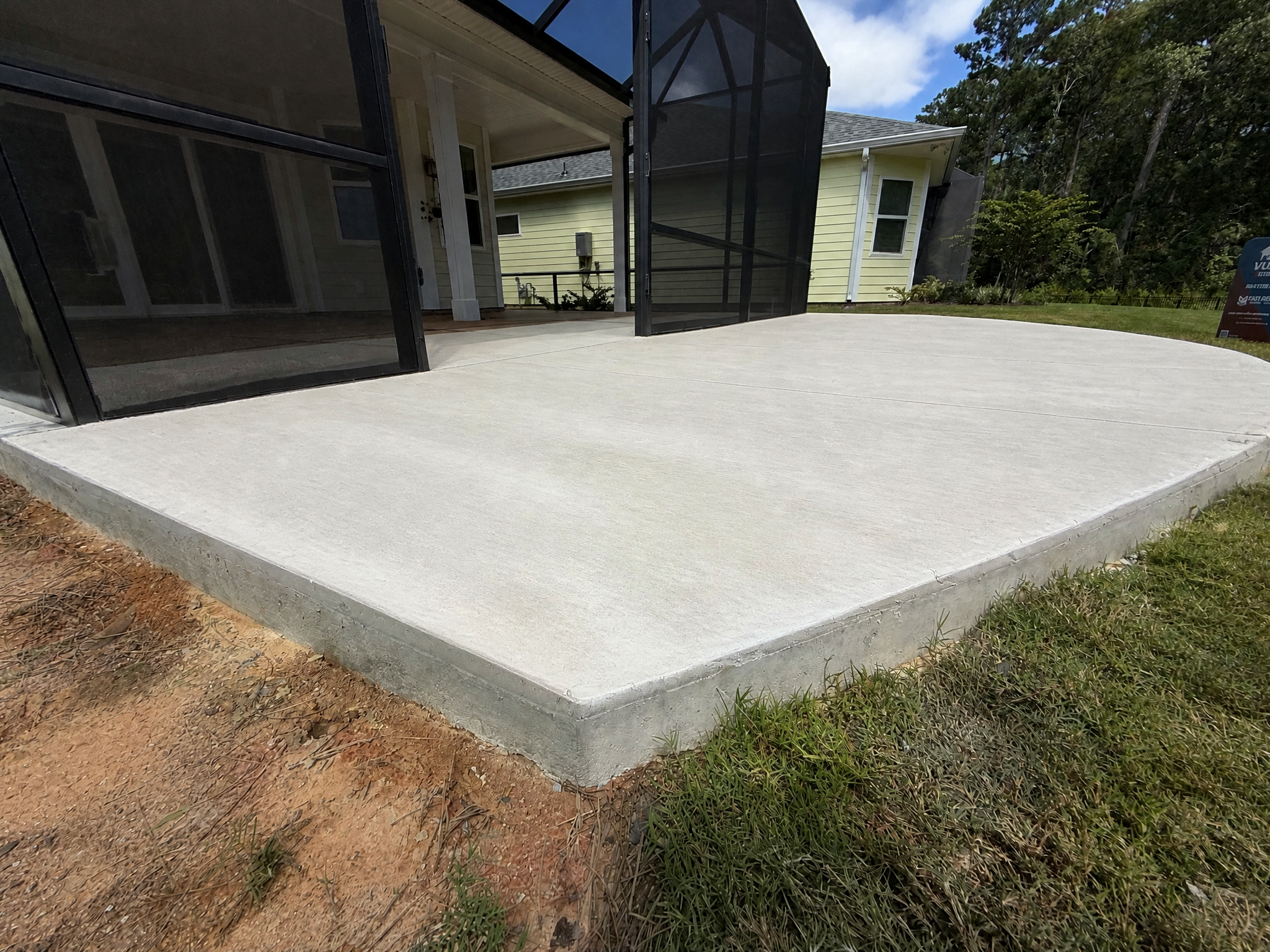 A newly finished concrete patio edge showcasing a smooth surface and surrounding grass in May River.