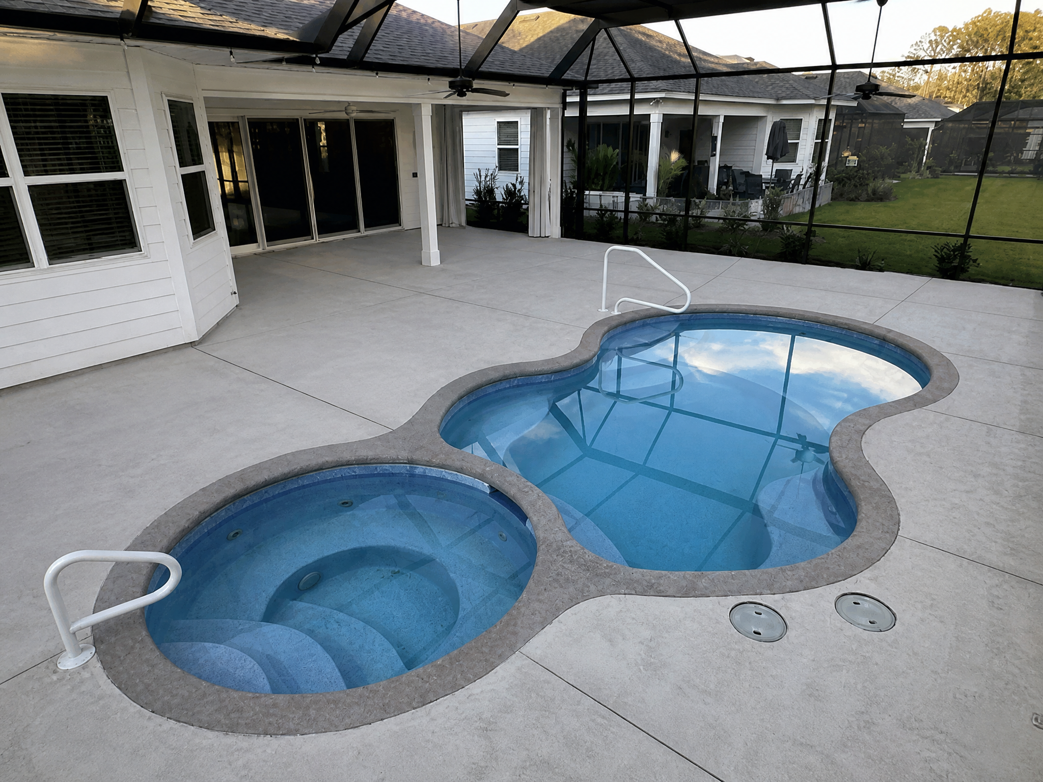A curved pool deck featuring a spa and a clear blue pool inside a screened enclosure.