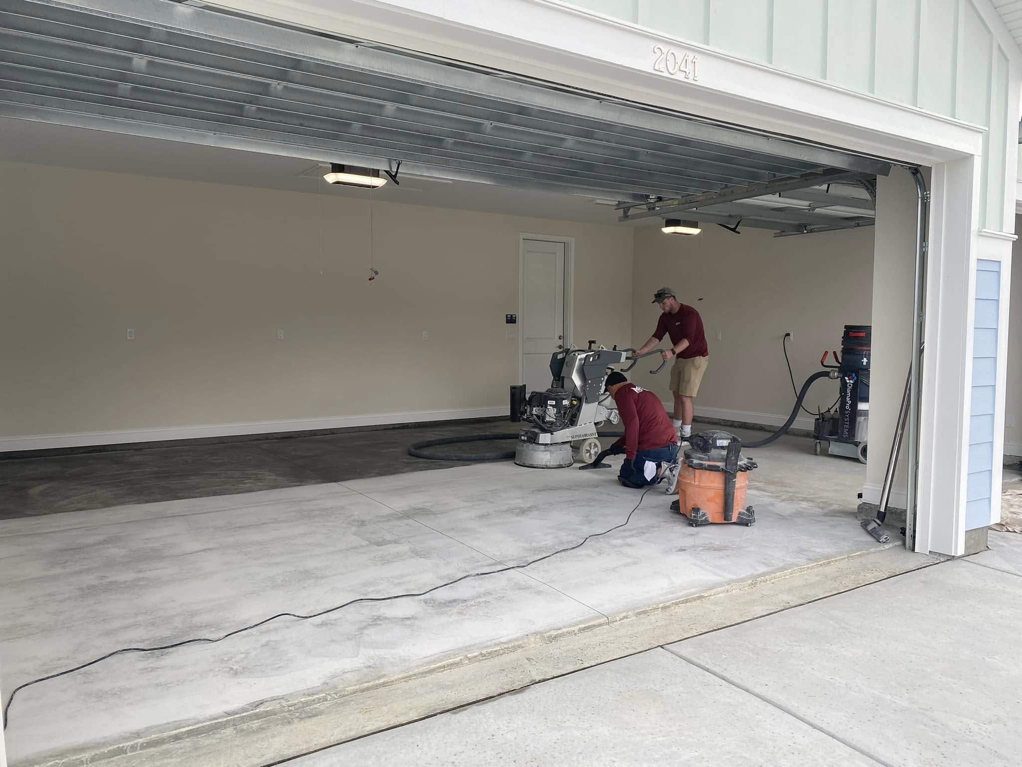 Two technicians working on a garage floor coating project with equipment in use.