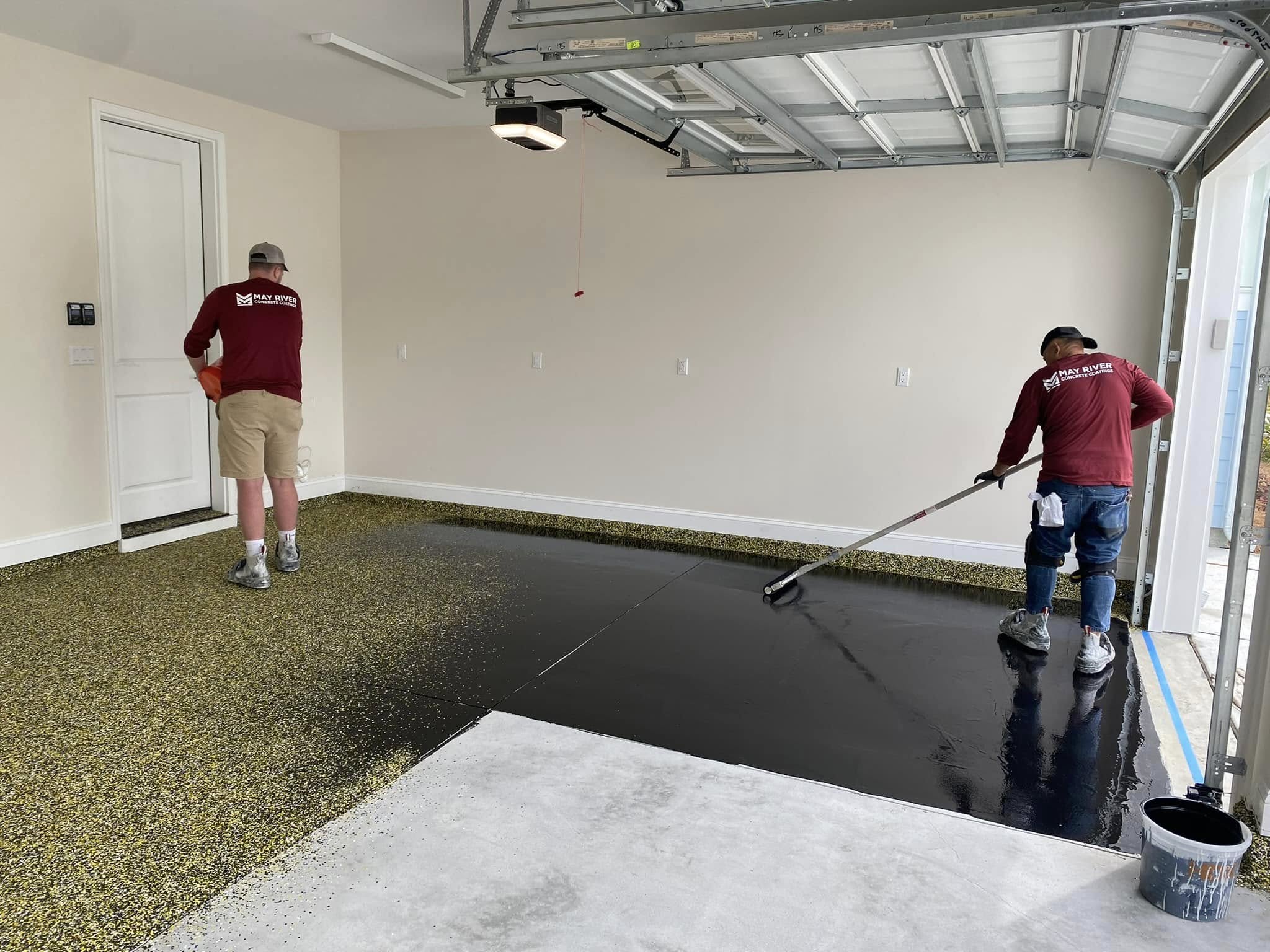 A worker applying a black coating to a garage floor for durability and protection.