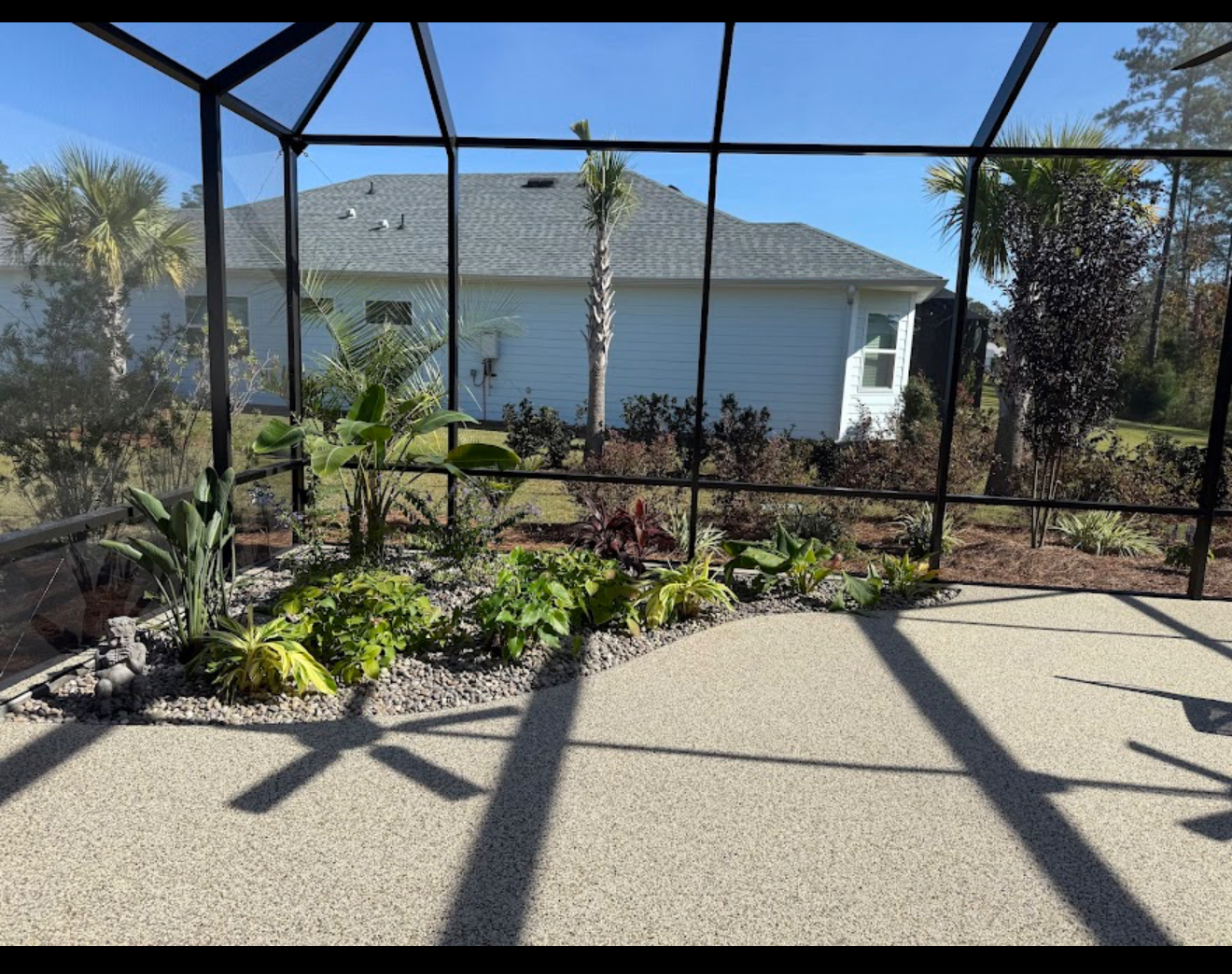 A screened enclosure featuring lush greenery and a patio area designed for coastal living.