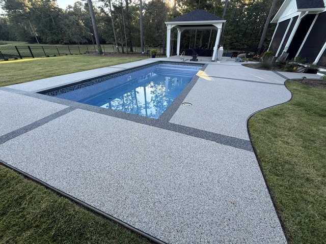 A vuba resin-bound pool deck surrounding a clear blue pool with a gazebo in the background.