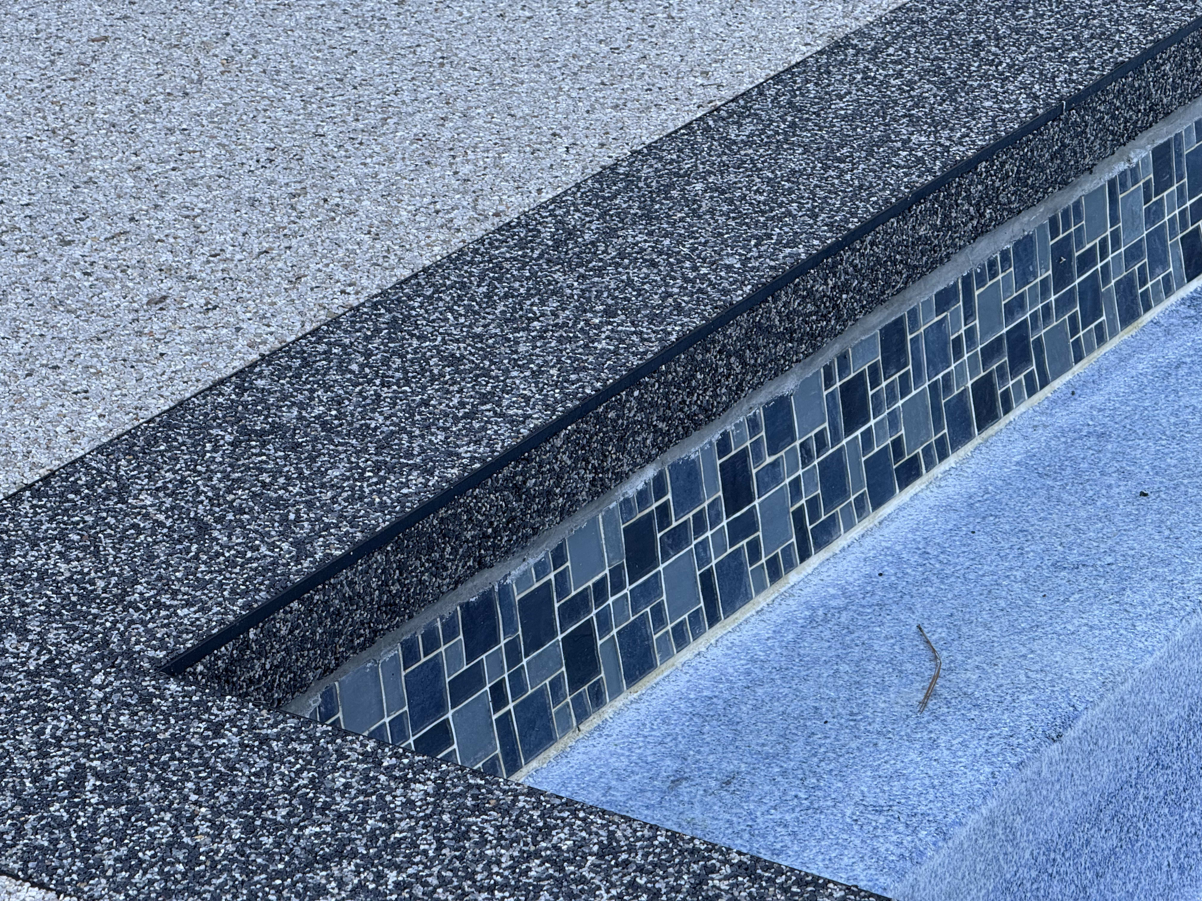Close-up view of a pool deck featuring Vuba Stone resurfacing and decorative tiles.