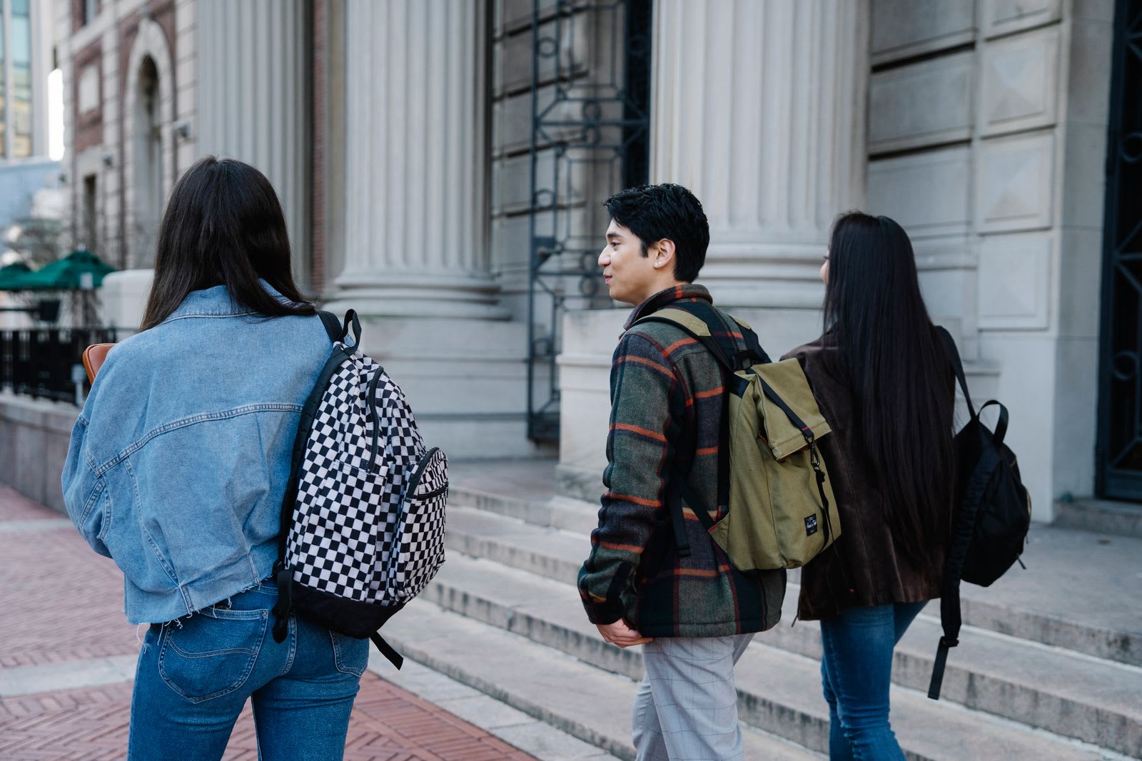 Three students with backpacks walking past the columns of a classical building in a European city