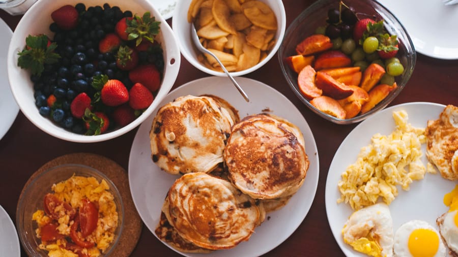 Different foods like eggs, muffins, strawberries, blackberries, tomatoes in separate plates on a white table