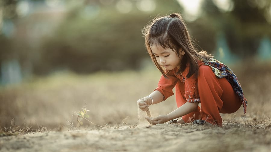 Vietnamese child in red outfit playing outdoors pouring sand through her fingers