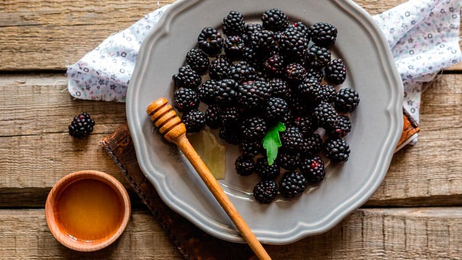 Blackberries on a plate and honey in a cup on a wooden table