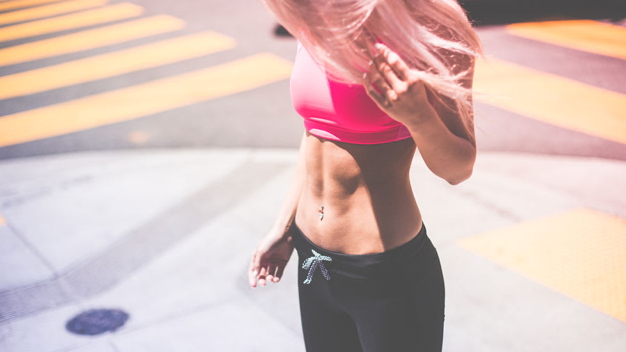 Woman in pink top and black drawstring pants on sidewalk with flat stomach