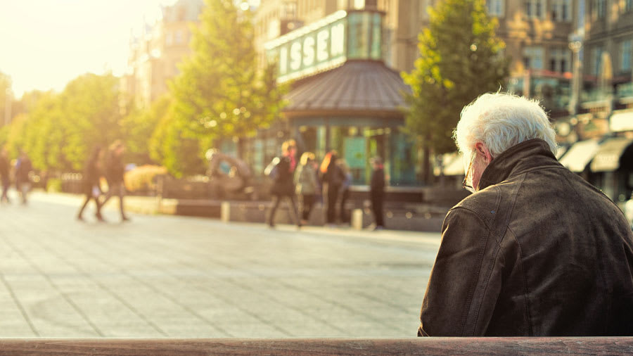 Old man with white hair wearing black leather jacket sitting on a park bench
