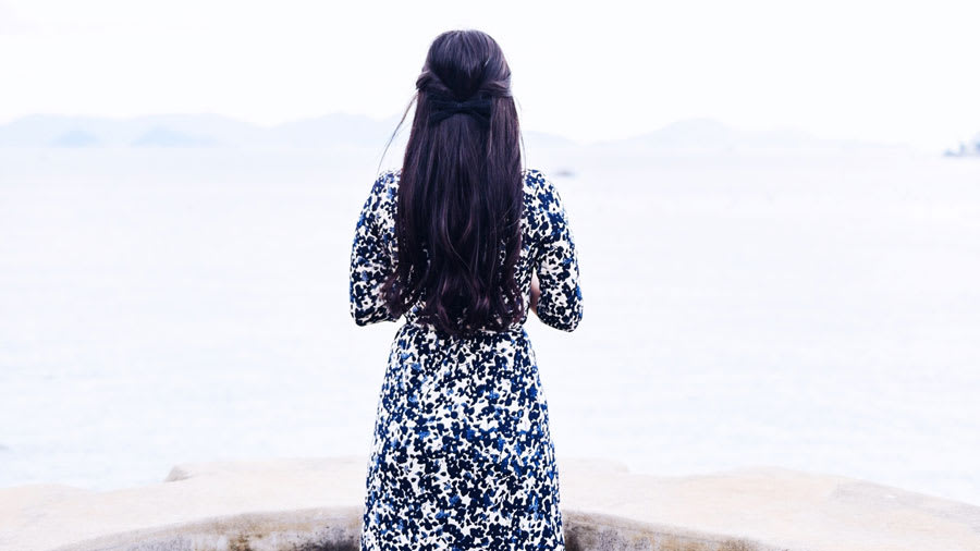 Woman with long black silky hair tied with a bow wearing a long blue and white floral dress