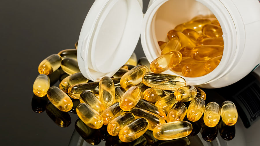Yellow supplement capsules spilling out of white bottle