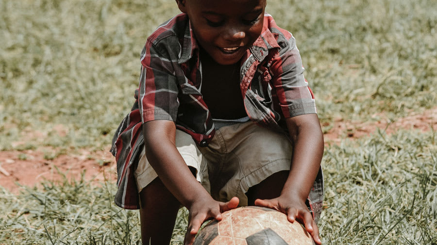 black-child-wearing-red-plaid-shirt-and-cargo-shorts-bending-down-to-play-with-soccer-ball