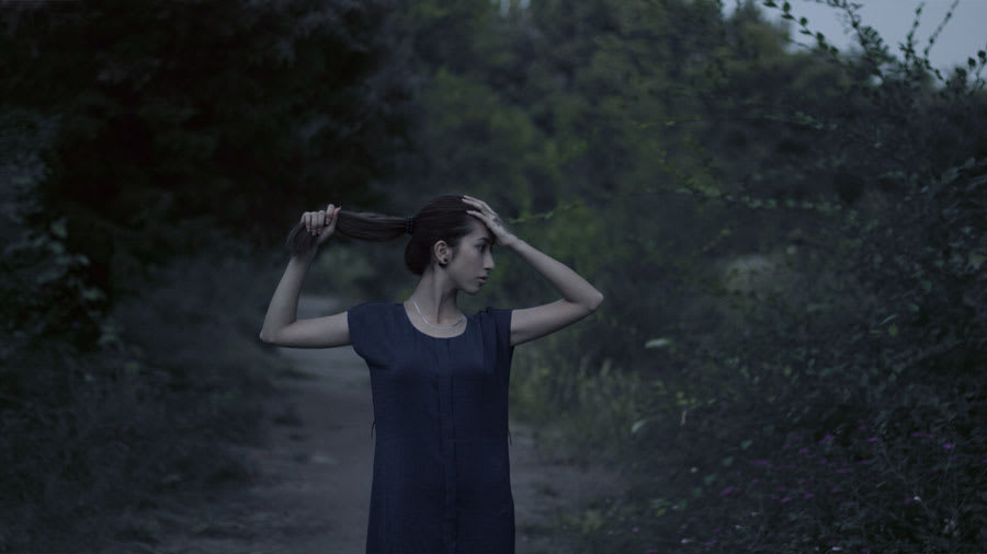 Woman standing outside on trail holding black hair looking gloomy