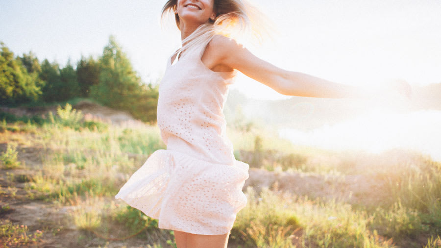 Woman wearing white dressing spinning outdoors with sun in background
