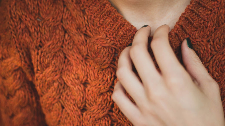 close-up of woman with dark green manicured nails wearing orange wool sweater scratching neck