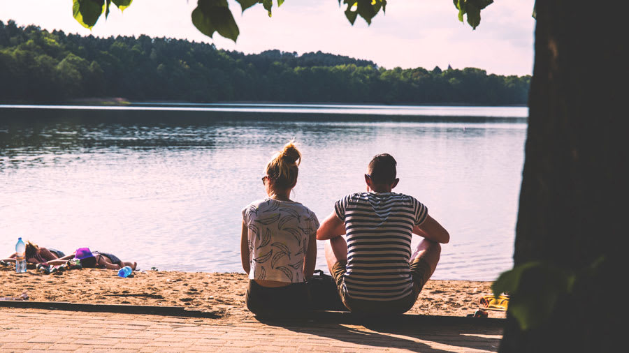Couple sitting in front of a lake next to a tree