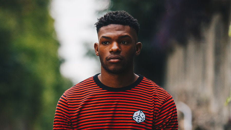 Young male in red and black striped shirt looking as if in deep thought with trees in background