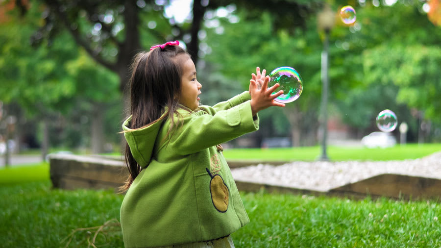 Asian girl wearing green jacket playing with bubbles in a park