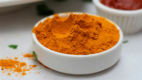 Turmeric in a white open container on the table with some spilled on the table