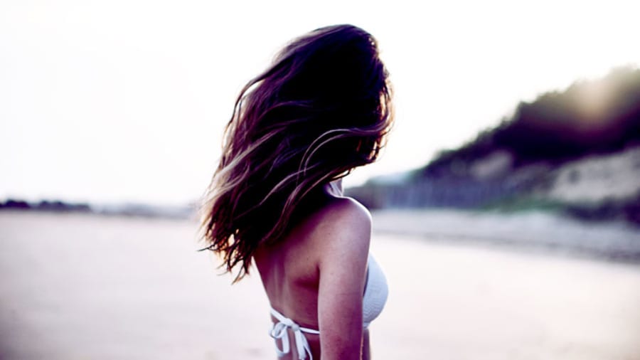 Beautiful brunette woman in white bikini on beach turned away from camera with beautiful skin