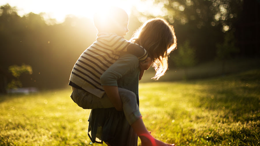 child getting piggyback ride on mother outside with sun shining on them.